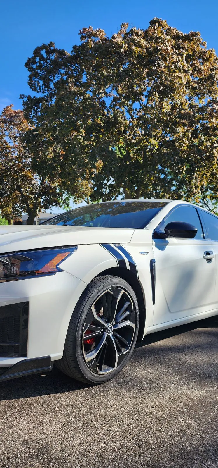Blue and black hash stripes on the front fender of a white Nissan Altima
